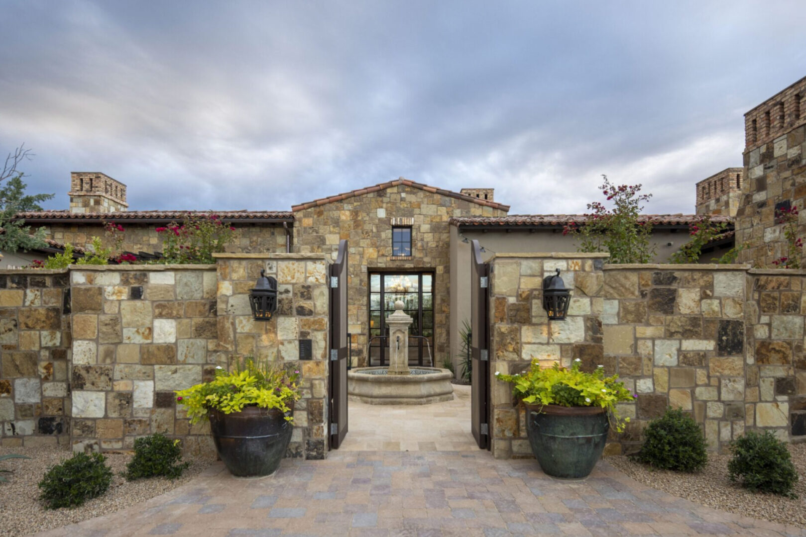 A stone wall with two doors and plants in front of it.