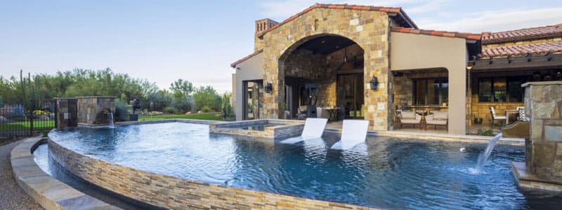 A pool with two chairs and a stone wall.