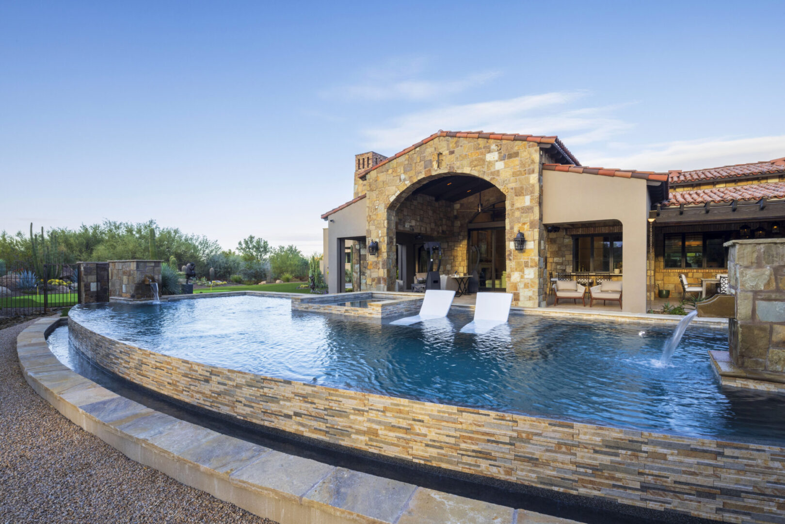 A pool with a large stone wall and a patio.