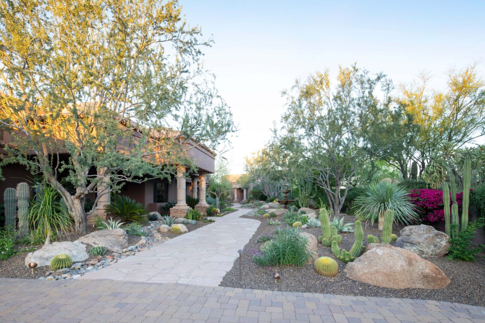 A walkway in front of a house with trees and bushes.