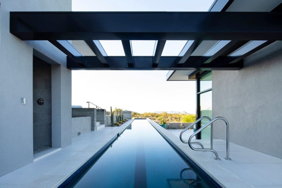 Modern outdoor swimming pool with sleek design, framed by minimalist architecture and metal beams. Scenic landscape view in the background.