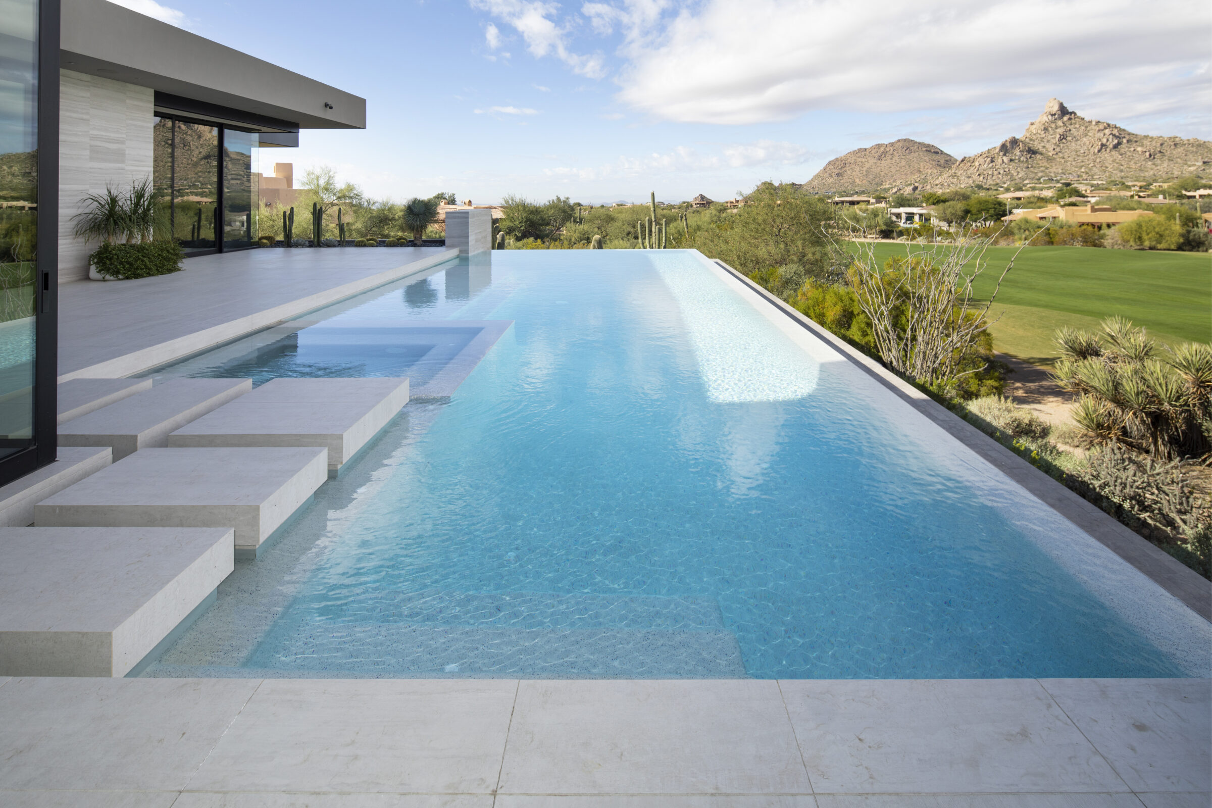 Modern house with infinity pool overlooking desert landscape and mountains. Clear sky, cacti, and minimalistic design create a serene and luxurious atmosphere.