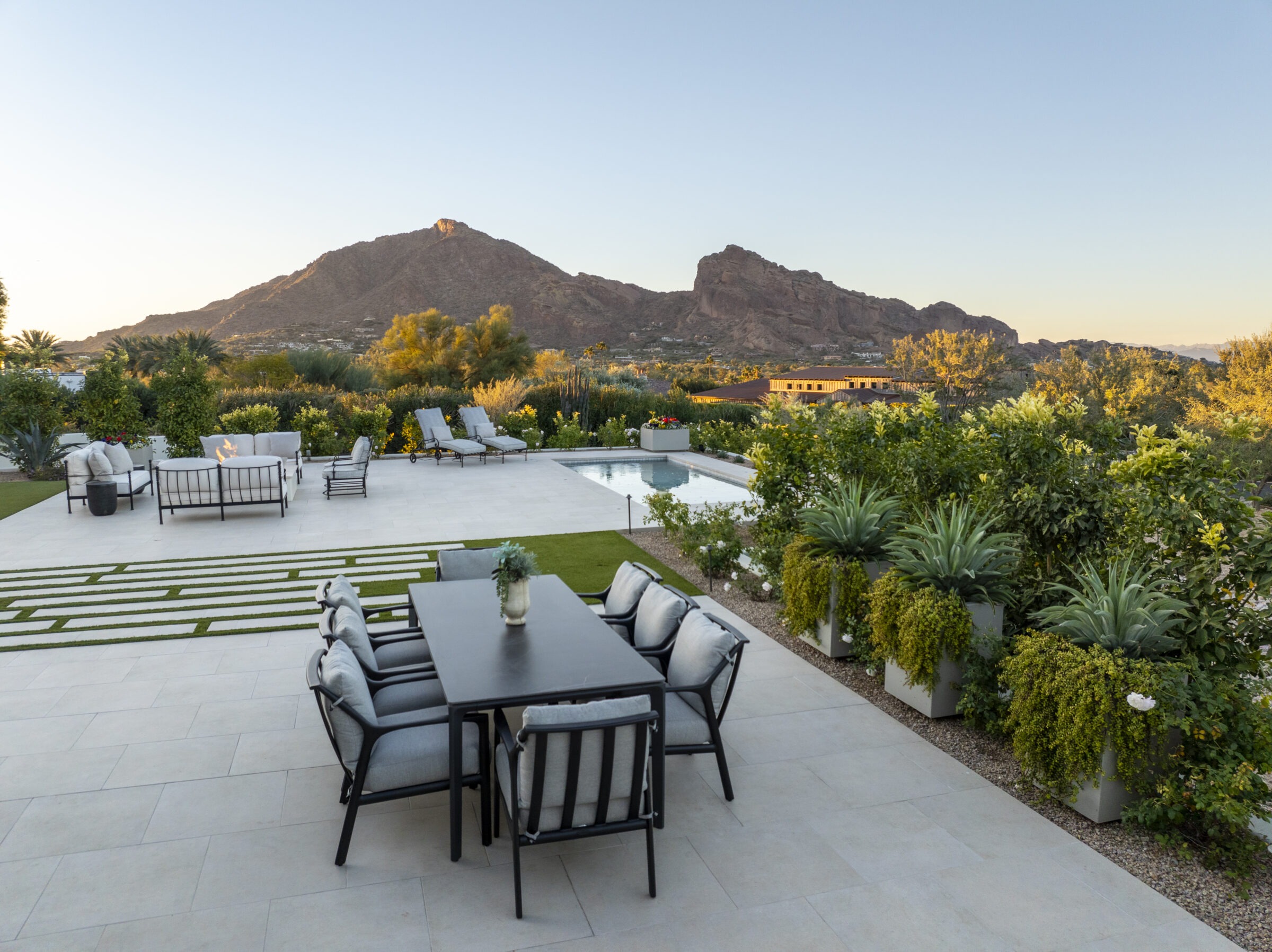 Modern patio with seating area and pool, surrounded by lush greenery. Camelback Mountain visible in the background at sunset, creating a serene atmosphere.