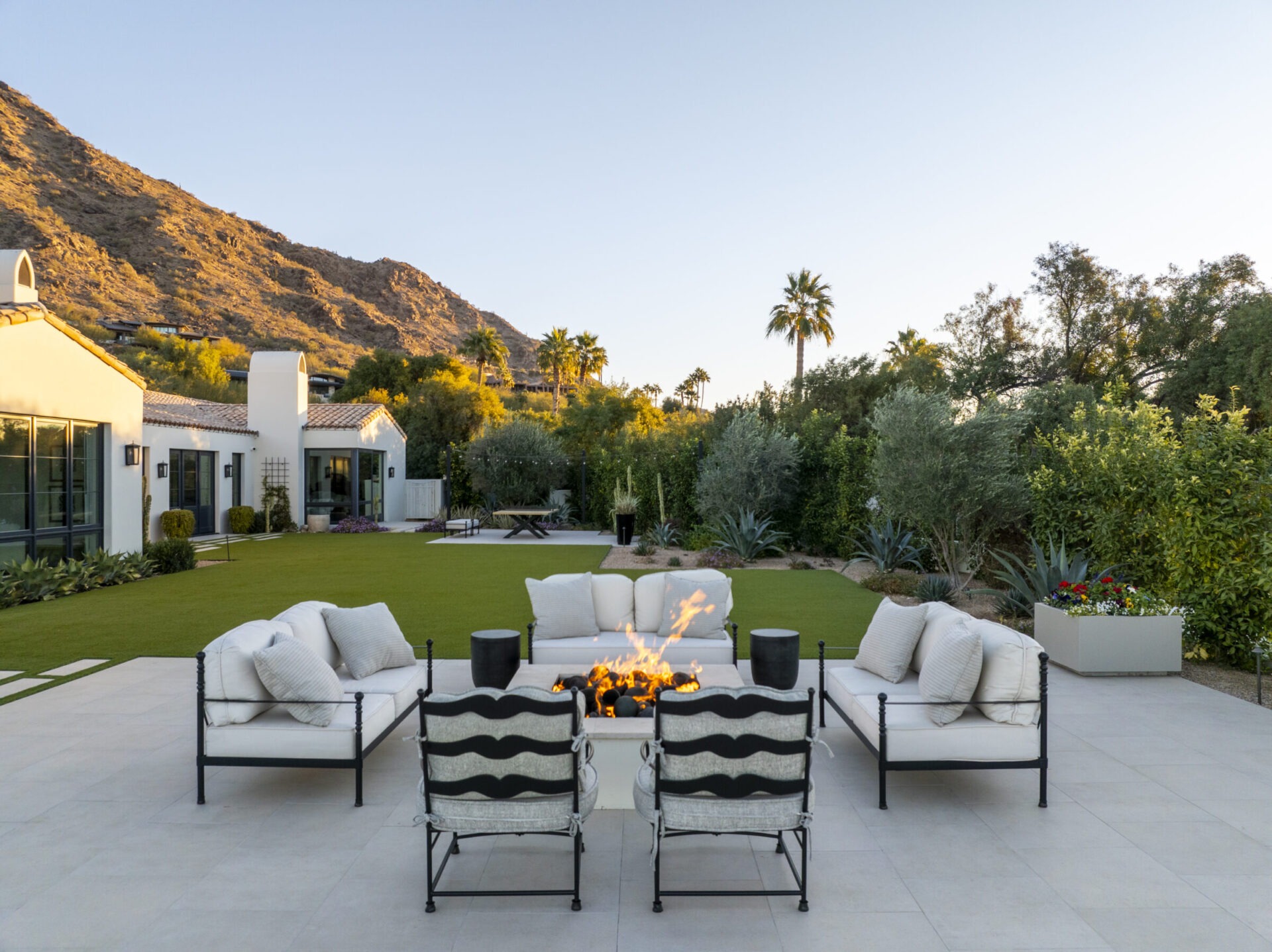 Modern patio with a fire pit, surrounded by cushioned chairs, desert landscape, and a view of a mountain in the background.