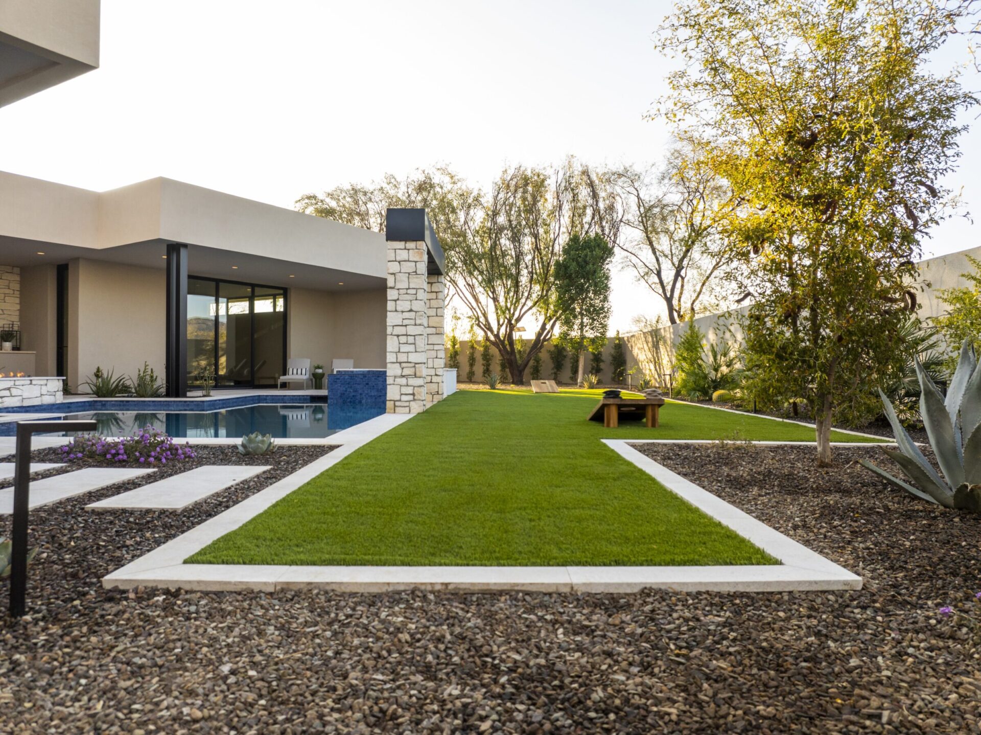 Modern house with sleek design, pool, and landscaped garden. Stone and glass elements enhance the outdoor space, featuring green lawns and desert plants.