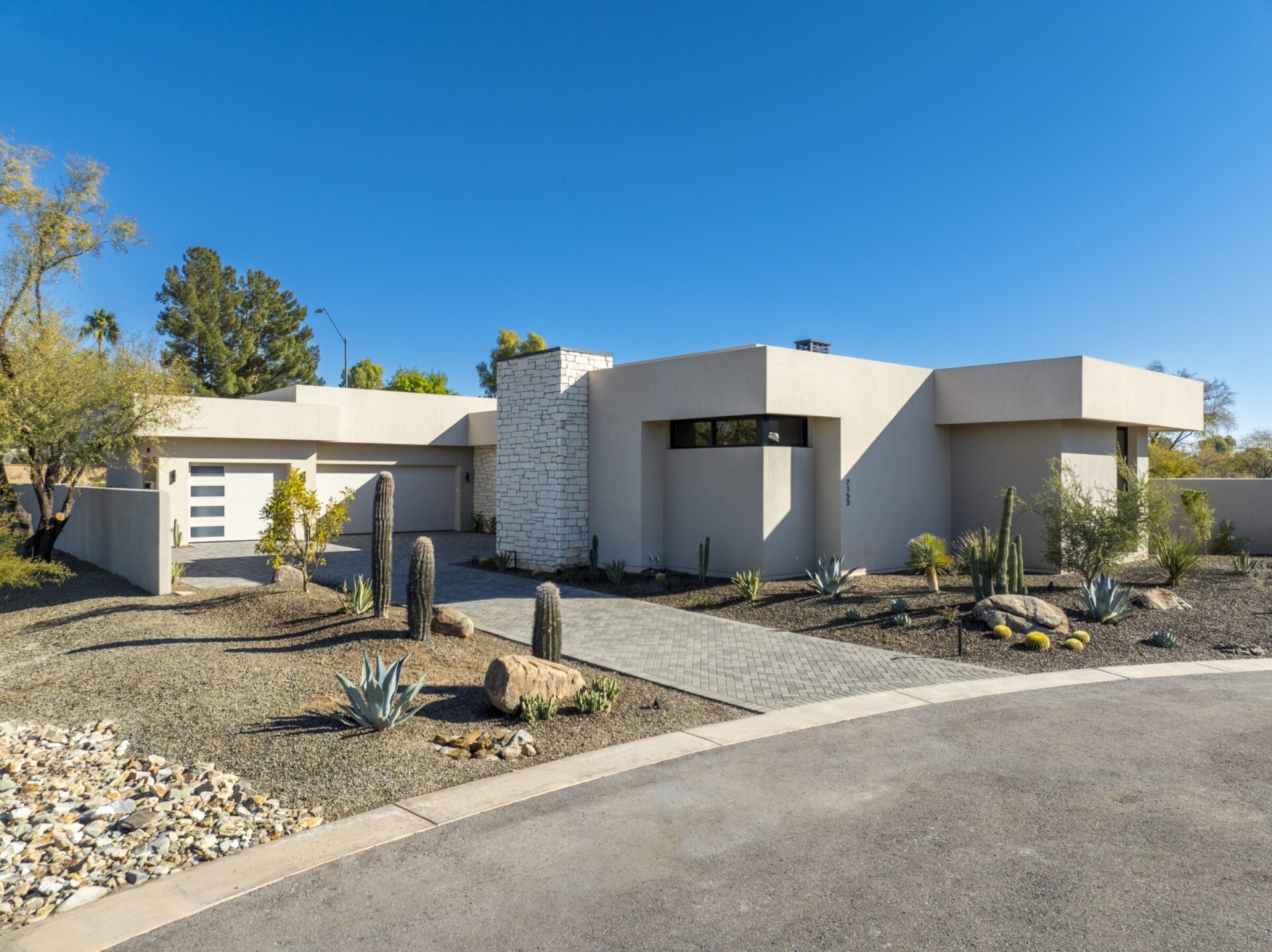Modern, single-story house with stone accents, surrounded by cacti and minimalist landscaping under clear blue skies, located in a suburban neighborhood.