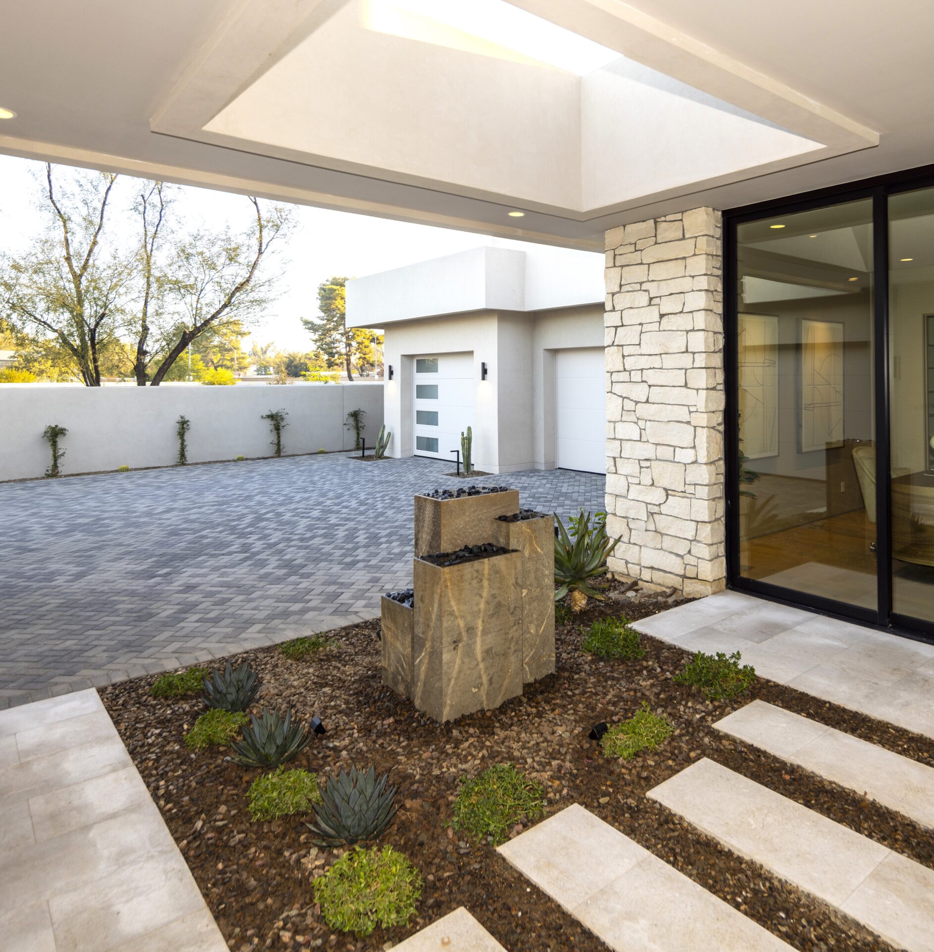 Modern courtyard with a geometric stone water feature, surrounded by minimalist landscaping. Features sleek architecture and large glass doors leading inside.