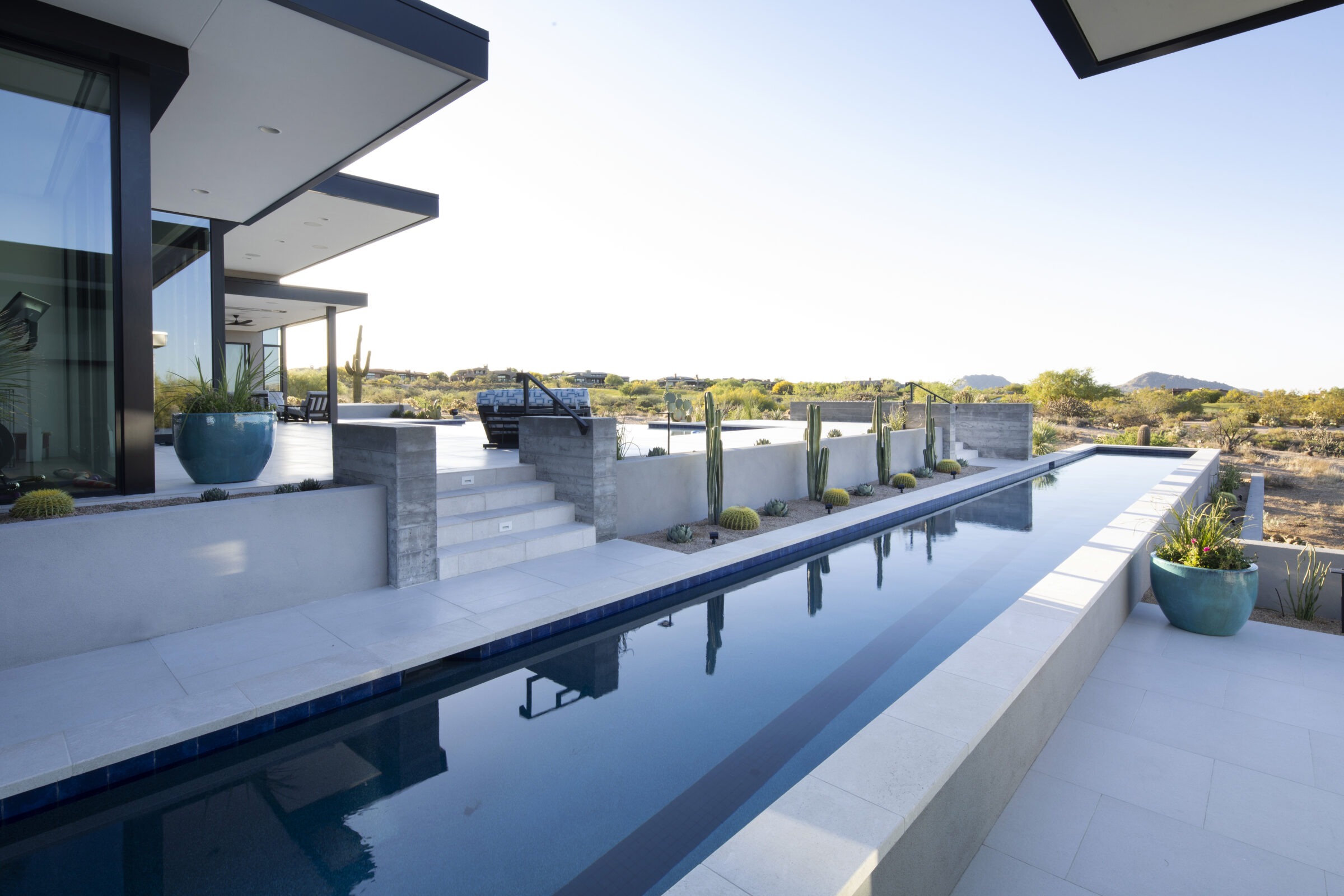Modern house with sleek design, pool, potted plants, and desert landscape featuring cacti. Spacious patio with serene views and minimalistic architecture.