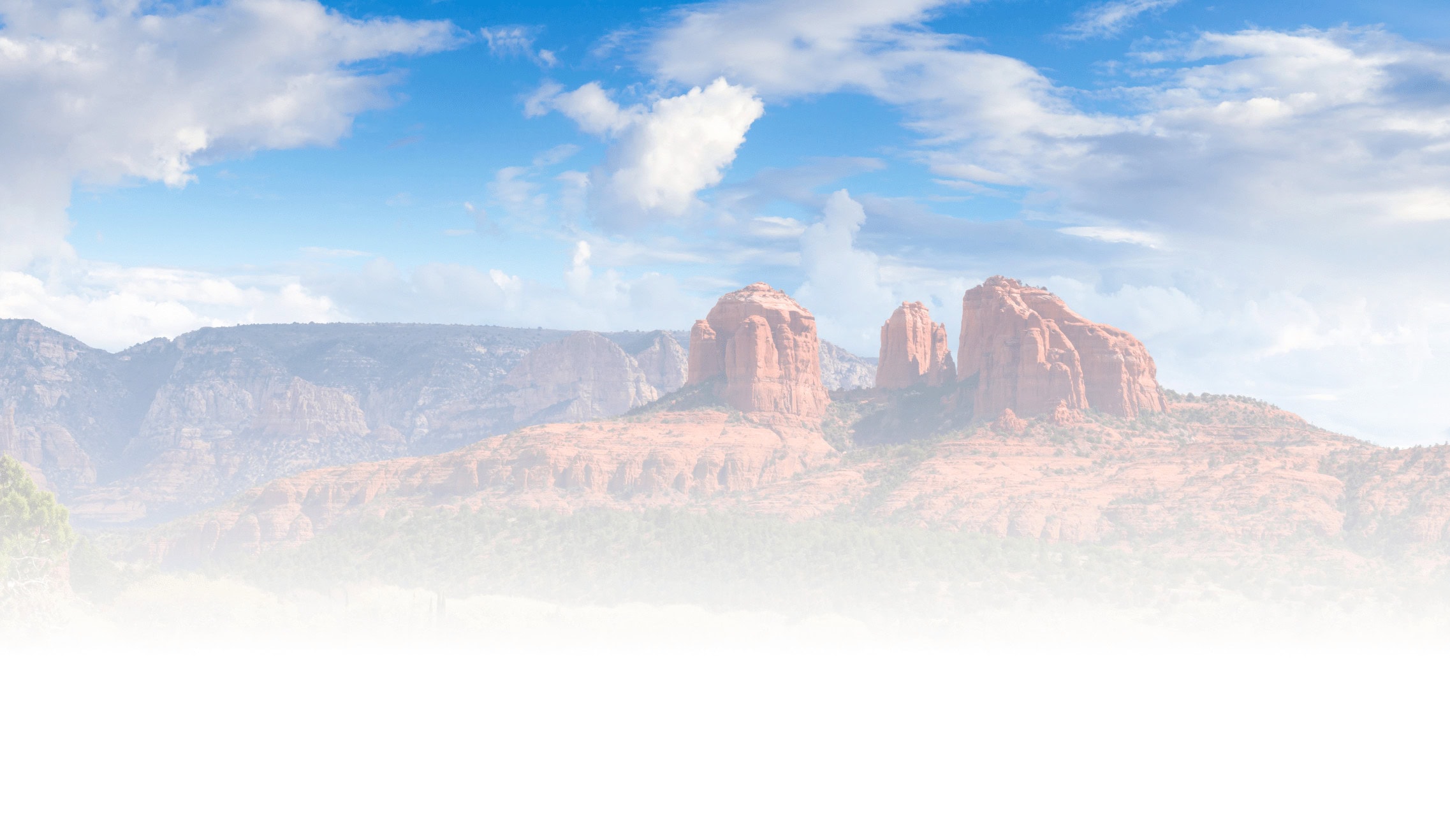 Red sandstone formations under a blue sky, resembling Cathedral Rock in Sedona, Arizona, with dispersed clouds and desert vegetation below.