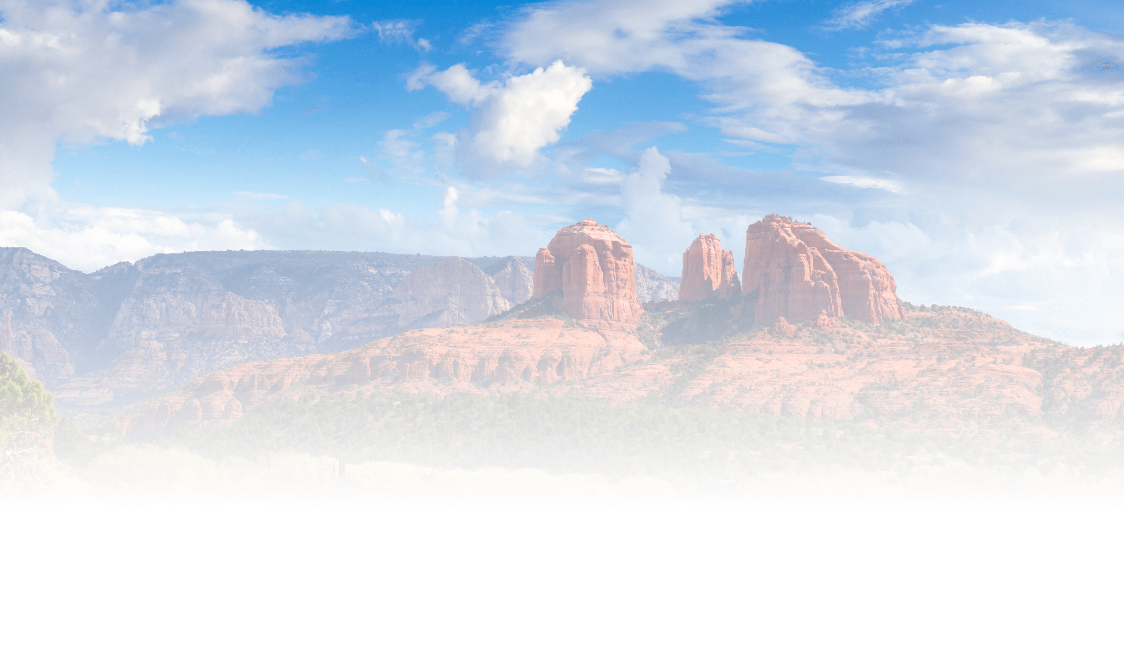 Red sandstone formations under a blue sky, resembling Cathedral Rock in Sedona, Arizona, with dispersed clouds and desert vegetation below.