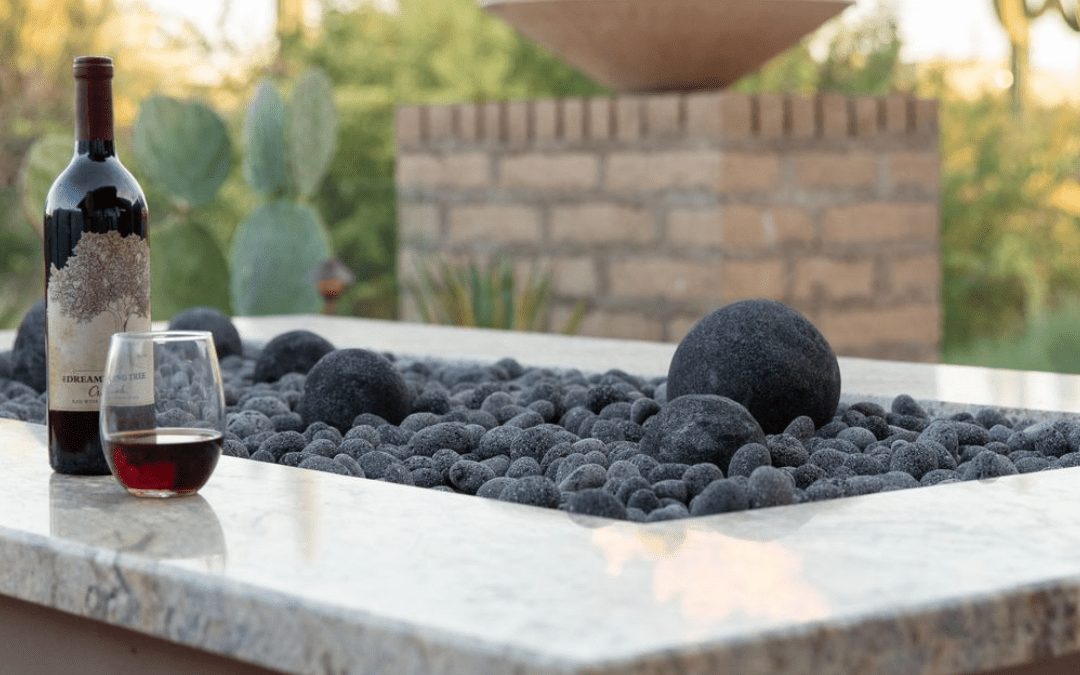 A wine bottle and glass on a stone table with cactus and brick wall in the background.