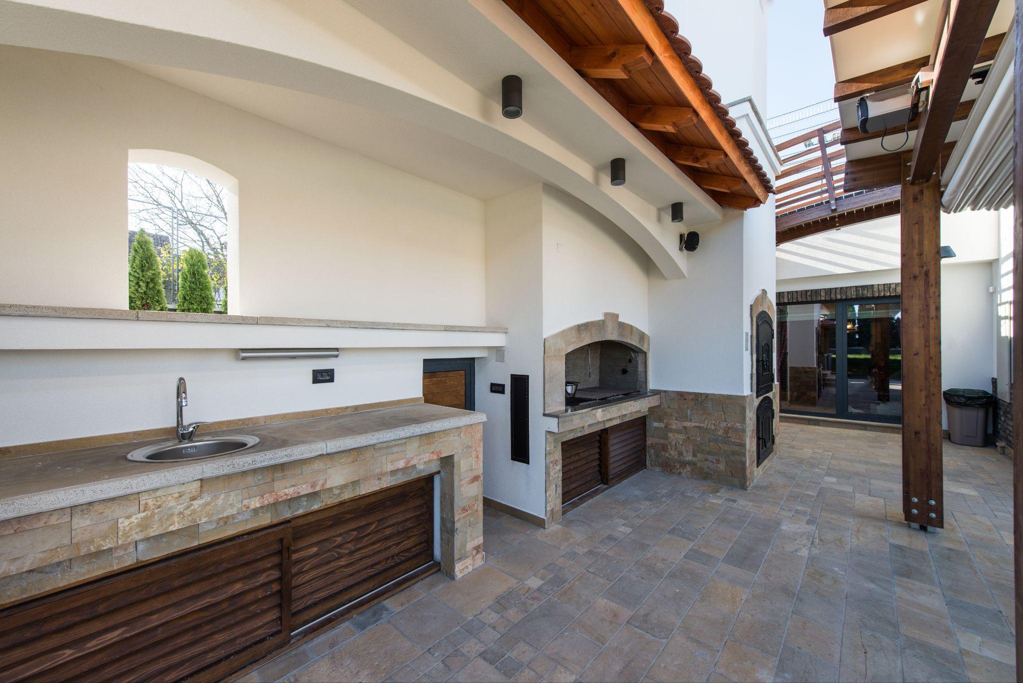 Outdoor kitchen with pizza oven, sink, stone finishes, and covered patio designed for entertaining in a desert climate